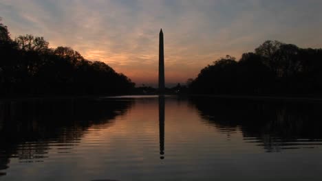 the washington monument in seen in silhouette and also in the reflecting pool