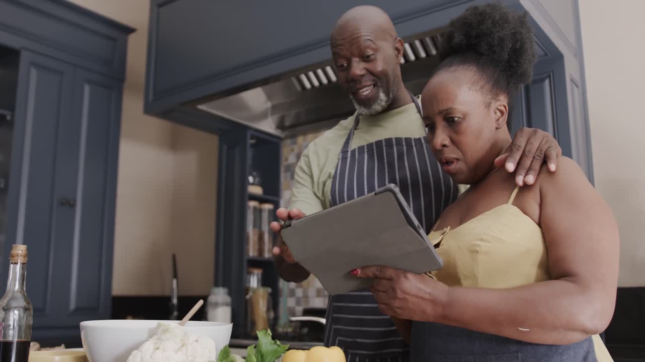 una feliz pareja afroamericana cocinando y usando una tableta en la cocina en cámara lenta
