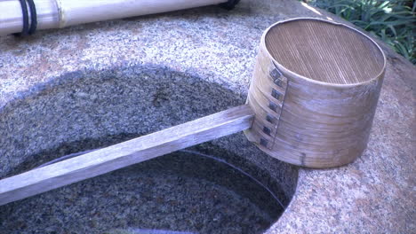 primer plano de un cucharón de bambú descansando sobre una cuenca de agua de lluvia en un jardín de té japonés