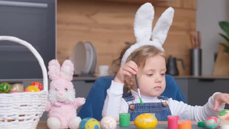 a little girl with easter bunny ears paints eggs with her family, preparing for the easter holidays. the scene captures the spirit of family fun, creativity, and the joy of the upcoming holiday