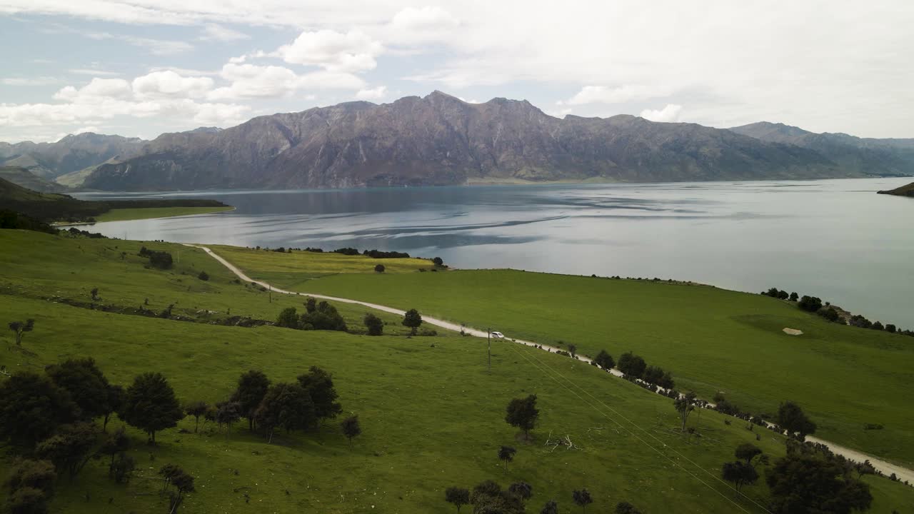 un hermoso día conduciendo un toyota estima a través de tierras de cultivo con lago y montañas en el fondo