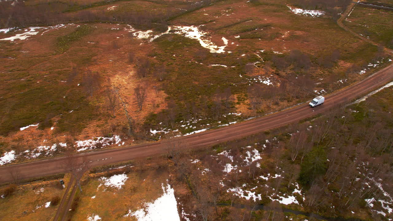 Aerial birdseye view of a van travelling along a dirt road in winter with small patches of snow on the ground