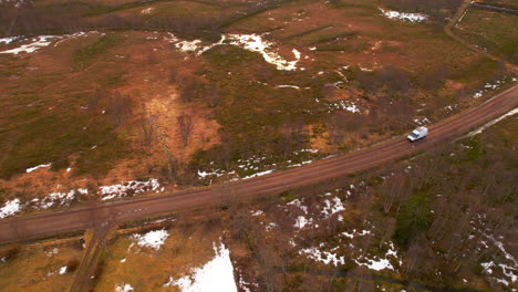 aerial birdseye view of a van travelling along a dirt road in winter with small patches of snow on the ground