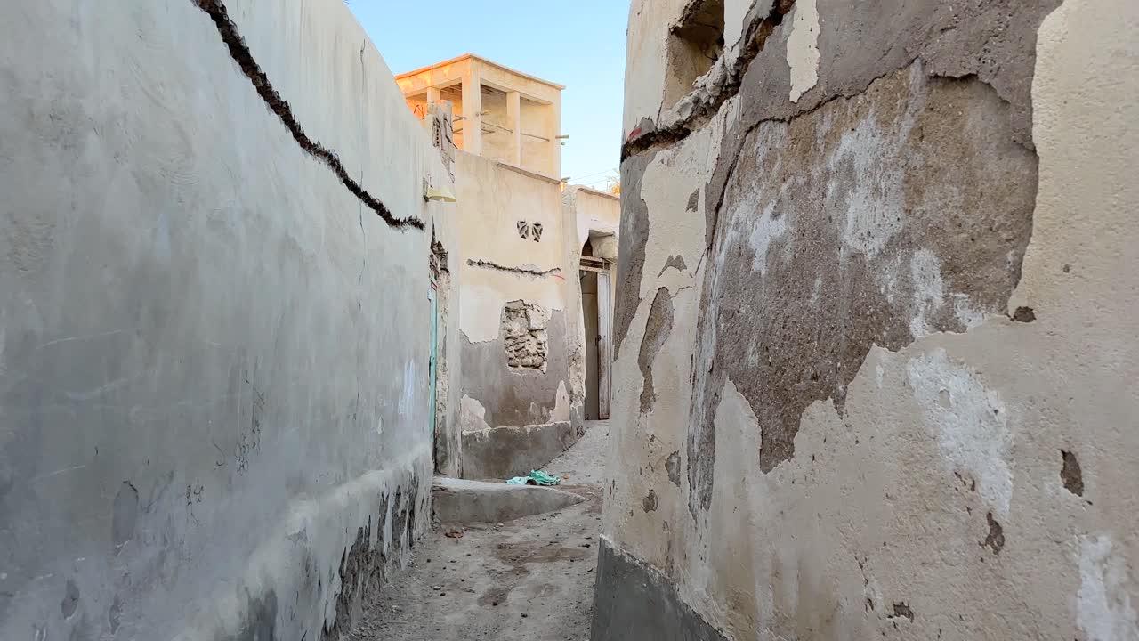 Passeggiando nel centro storico di una città desertica, clima tropicale, rovine di case in mattoni di fango, cultura araba, design architettonico tradizionale, vicolo tortuoso, catturavento, antica ventilazione naturale, flusso d'aria, casa storica.