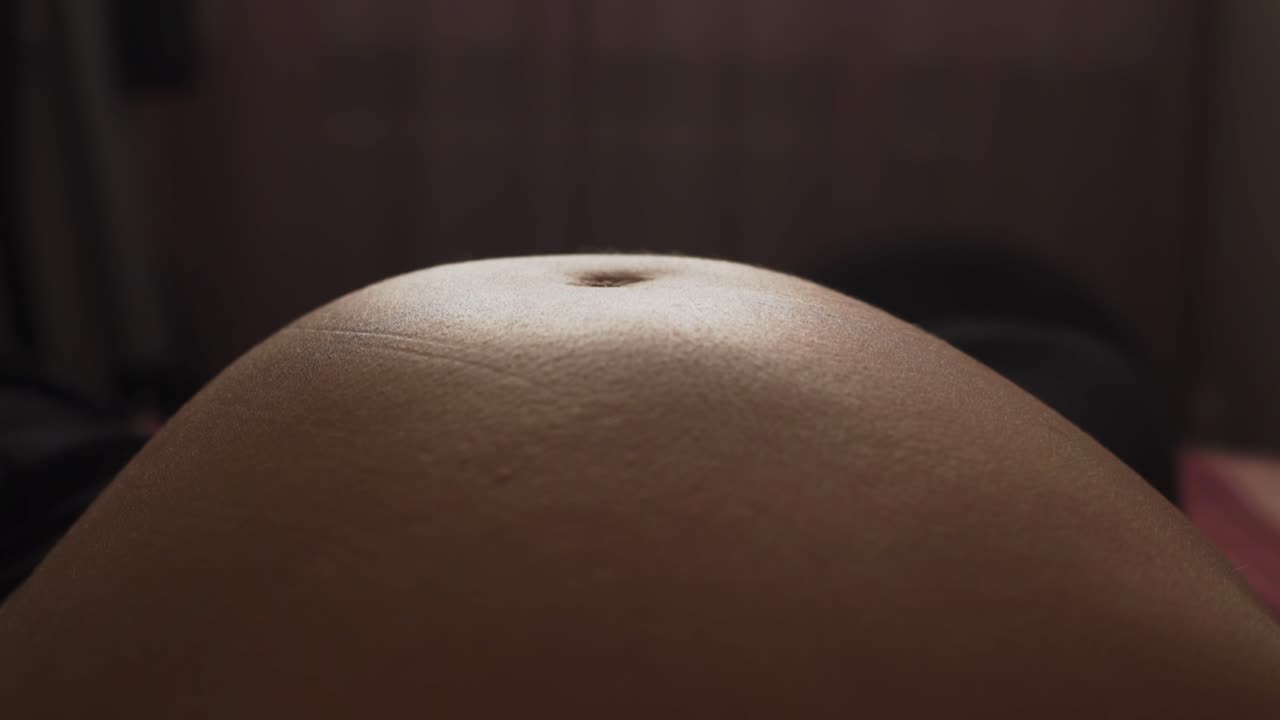 Primo piano del ventre di una donna incinta che mostra i sottili movimenti, i rigonfiamenti e i calci di un bambino non ancora nato, enfatizzando la crescita di una nuova vita e il processo naturale della gravidanza e dell'attesa
