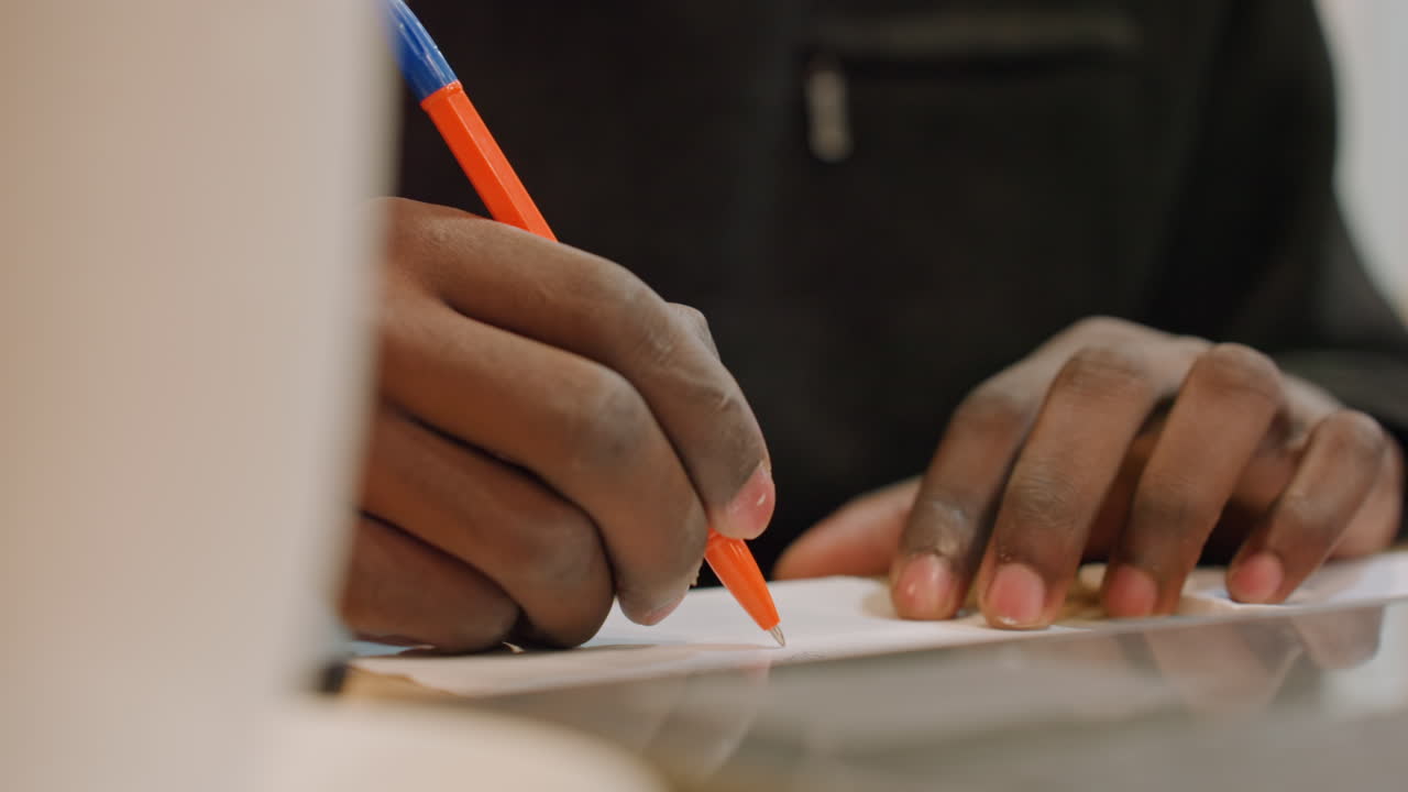 Nærbillede af hænder der skitserer med orange pen på bordet, kreativ designer udarbejder layout ved siden af bærbar computer, fokuseret studiestemning, detaljeret stregarbejde, hurtige konceptnoter og visuel udforskning.