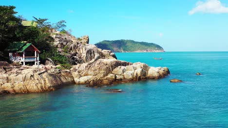 Colorful-beach-cabins-over-rocky-coastline-of-tropical-island-washed-by-calm-azure-sea-water-under-bright-blue-sky-in-Thailand