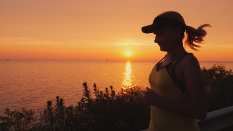 a young woman runs in a picturesque place by the sea where the sun sets over the water