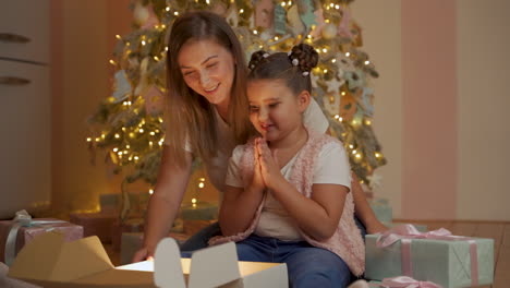 Niña-Y-Mujer-Abren-Caja-De-Regalo,-Sale-Luz-Dorada,-Se-Sorprenden