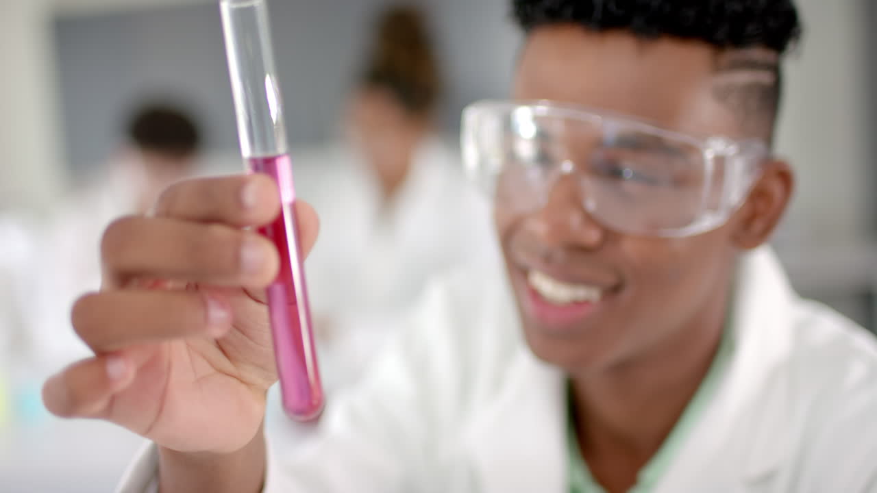 Teenage biracial boy examines a test tube in a high school laboratory
