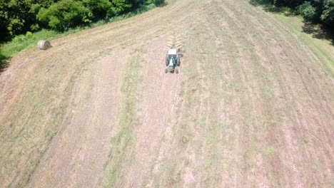 vista aérea de drones del tractor tirando de un rastrillo a través de un campo de heno para hacer hileras para empacar más tarde en el oeste de illinois a principios del verano