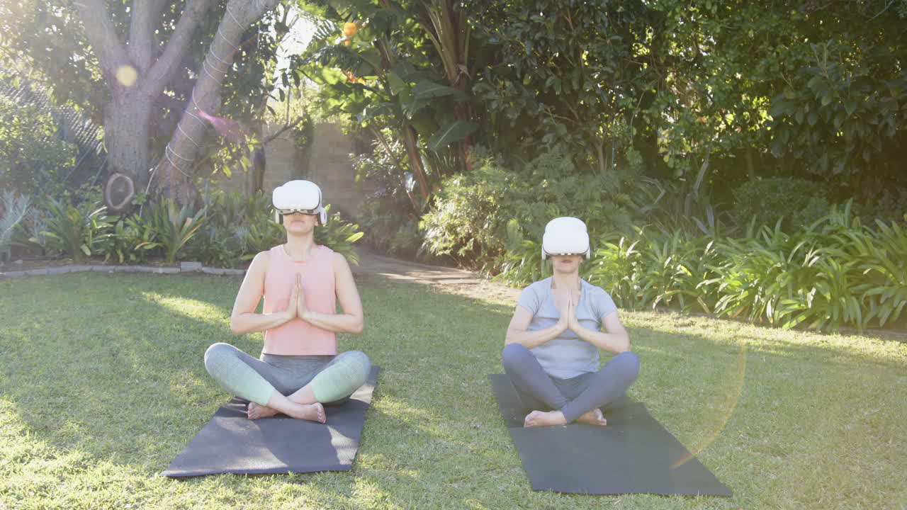 In garden, women practicing yoga using VR headsets on mats outdoors