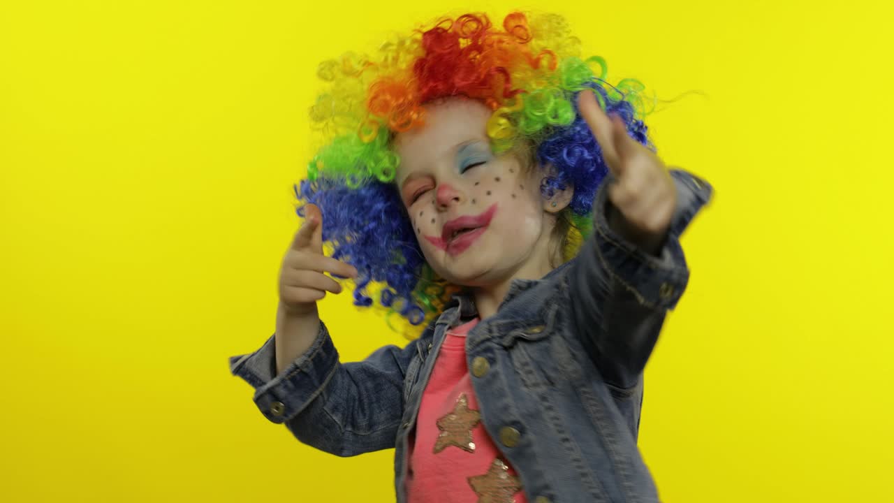 niña pequeña payaso en peluca colorida haciendo caras tontas, tonto alrededor, sonriendo, bailando. halloween