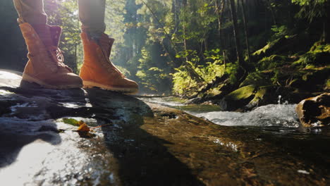 the feet of the traveler stand on a wet log near a mountain stream tourism and hiking conceptt