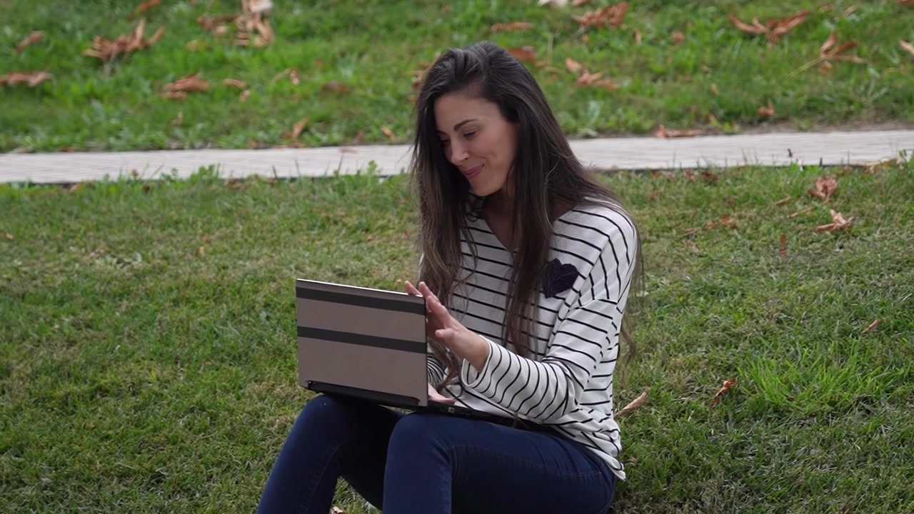 Una giovane donna sta lavorando diligentemente al suo laptop in un bellissimo ambiente naturale all'aperto.