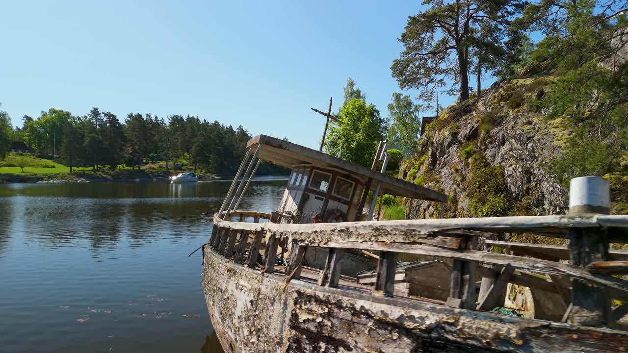 Opuštěná, chátrající dřevěná loď stojí v mělké vodě jezera v Köpmannebro ve Švédsku. Vzdušný záběr z dronu ukazuje zrezivělé textury a přirozený rozklad.