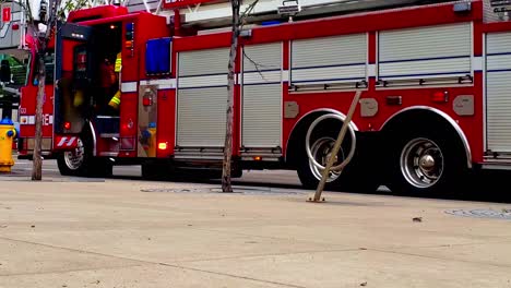 1-2red fire truck parked in a downtown city next to a yellow fire hydrant with blue caps and firefighter at the back door of the 2nd row entering into the vehicle sorting supplies needed