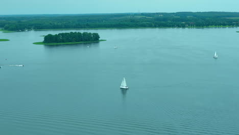 aerial view of sailboats gliding on the expansive waters of jeziorak lake, with a small island in the distance, offering a serene and picturesque scene of outdoor adventure