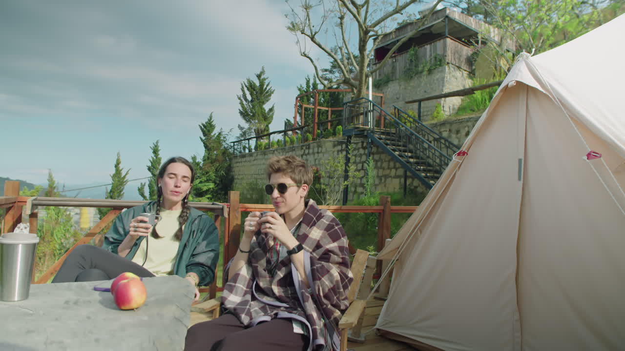 Two Female Friends Relaxing at Glamping in Mountains and Chatting over Tea