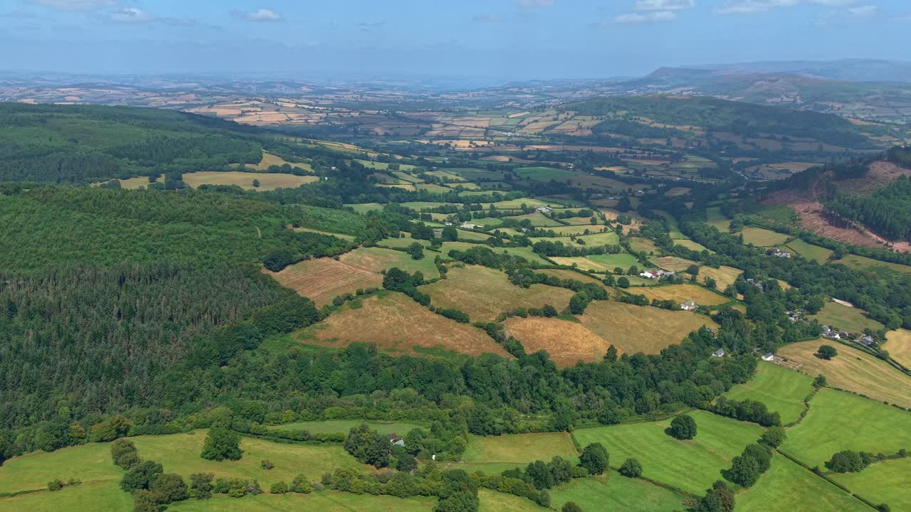 Aerial drone footage flying backward over rolling farmland and forests in Brecon Beacons