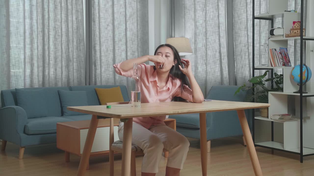 술에 취한 아시아 여성이 보드카를 마시며 집에서 카메라를 쳐다보고 있습니다.