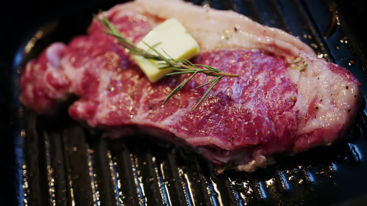 Butter melting on a seasoned steak cooking on a hot grill pan with rosemary herbs