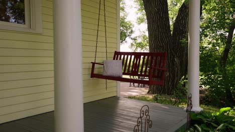 orbiting shot of a red hanging swing on the front deck of a farmhouse