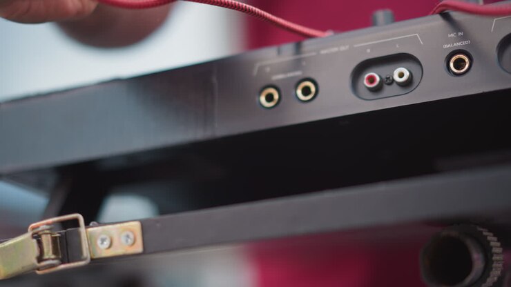 Primo piano di jack audio e cavo inseriti manualmente in una custodia per mixer portatile, cavo rosso intrecciato che passa attraverso una chiusura metallica, profondità di campo ridotta, luce soffusa da studio, movimento tattile intimo.