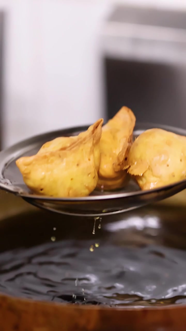 Samosa dorati sollevati dall'olio bollente in un wok di ottone usando una schiumarola metallica