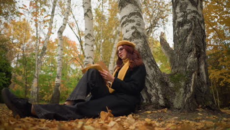 young lady sits under tree in solitude, reading book thoughtfully in autumn forest, surrounded by golden leaves, she embraces calm, inspiration, and creativity in a peaceful outdoor retreat