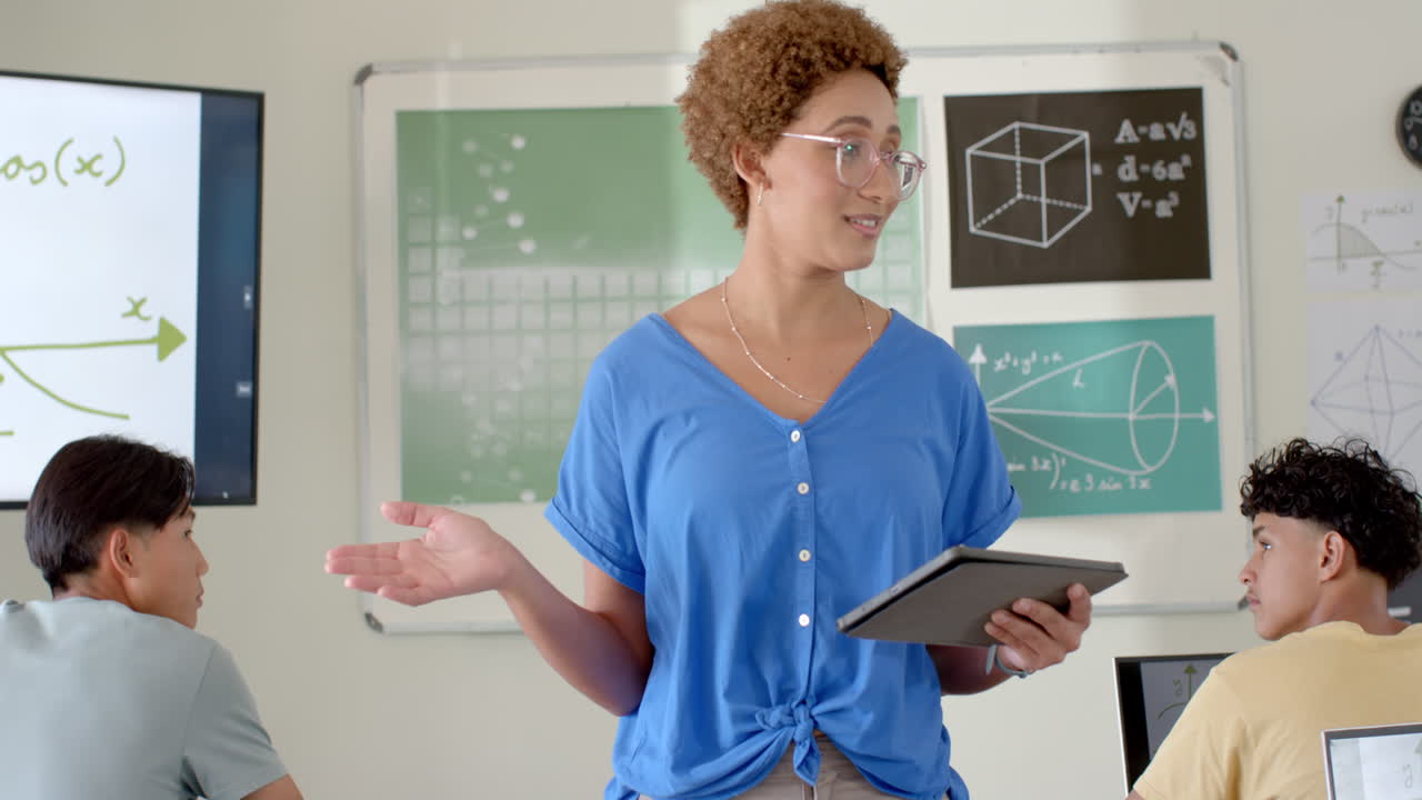 Teaching math, teacher holding tablet and explaining concepts to students in high school