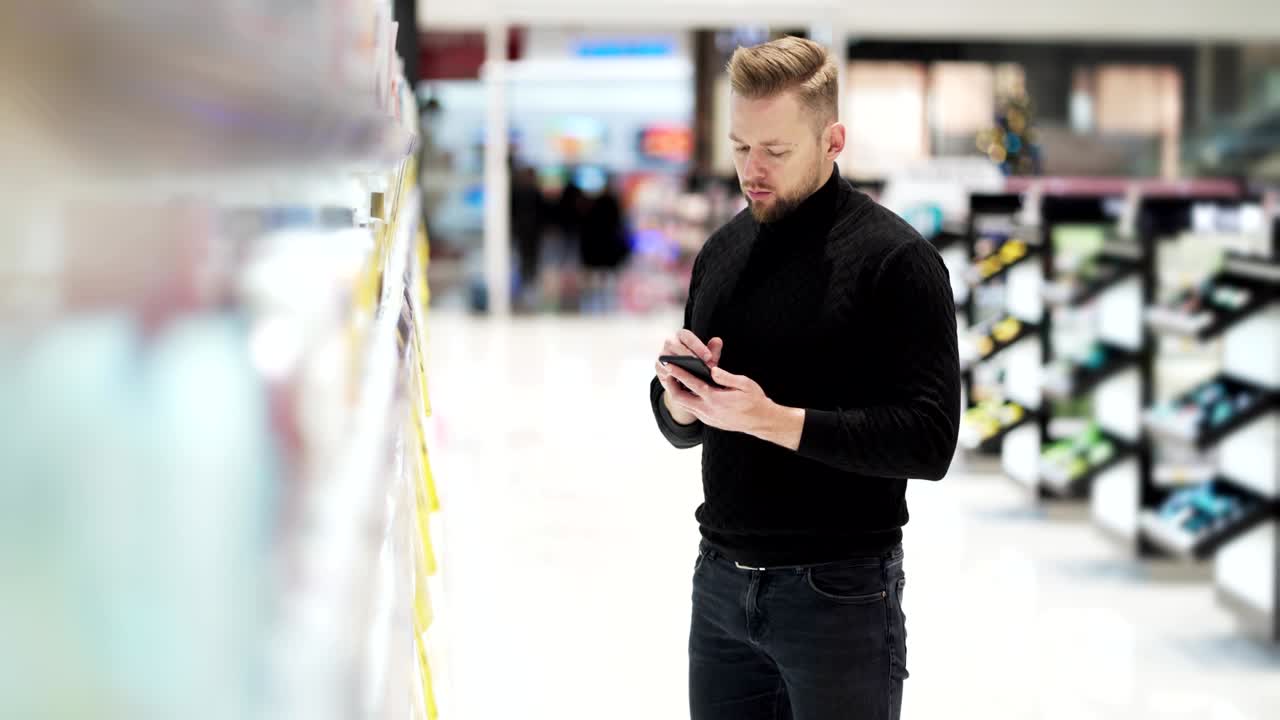 Young bearded man talking on phone and selects product in cosmetics store