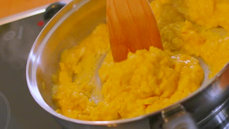 cooking scrambled eggs in frying pan with wooden spatula stirring with hot steam rising in slow motion on electric cooker hob. healthy breakfast footage.