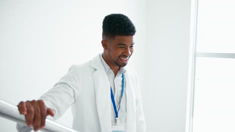 portrait of smiling male doctor wearing white coat standing on stairs in hospital