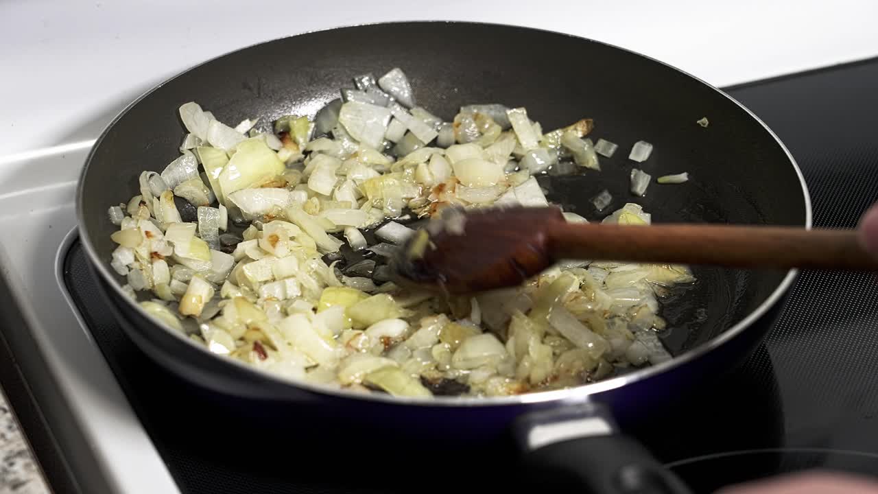 Cipolle tritate vengono cotte in una padella sul fornello. Una mano mescola le cipolle, rendendole morbide e dorate. Questo è un passaggio comune in molte ricette.
