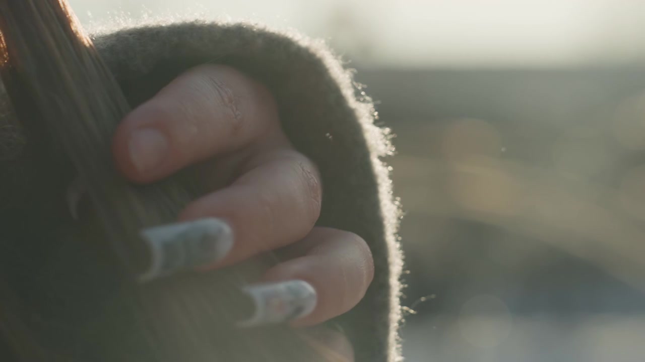 Quiet moment capturing tender hand gesture. Closeup of delicate fingers under warm sunlit light. Artistic depiction of peaceful hands engaging in gentle hair twirling under soft sunlight