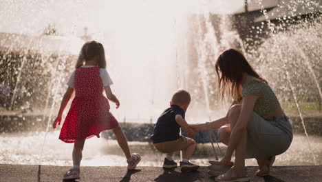 Playful-little-children-with-mother-have-fun-near-fountain