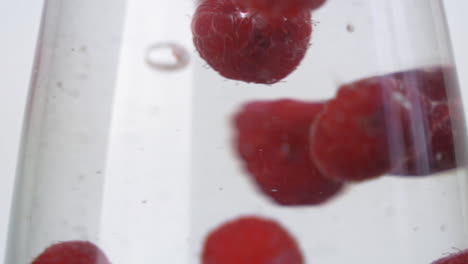 slow motion bright red raspberries splashing into cold glass of water up close