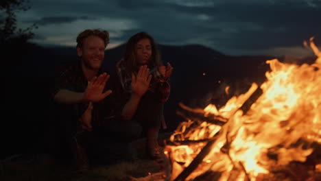 resting couple warm hands on night campfire closeup. two travelers enjoy bonfire