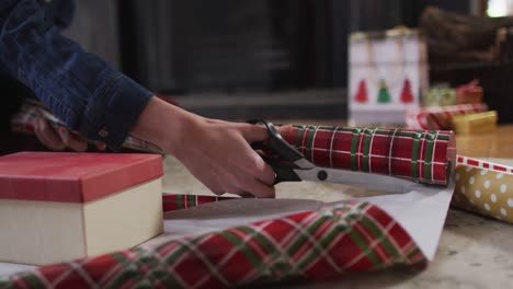 sección media de la mujer cortando papel de embalaje para regalos de navidad en casa