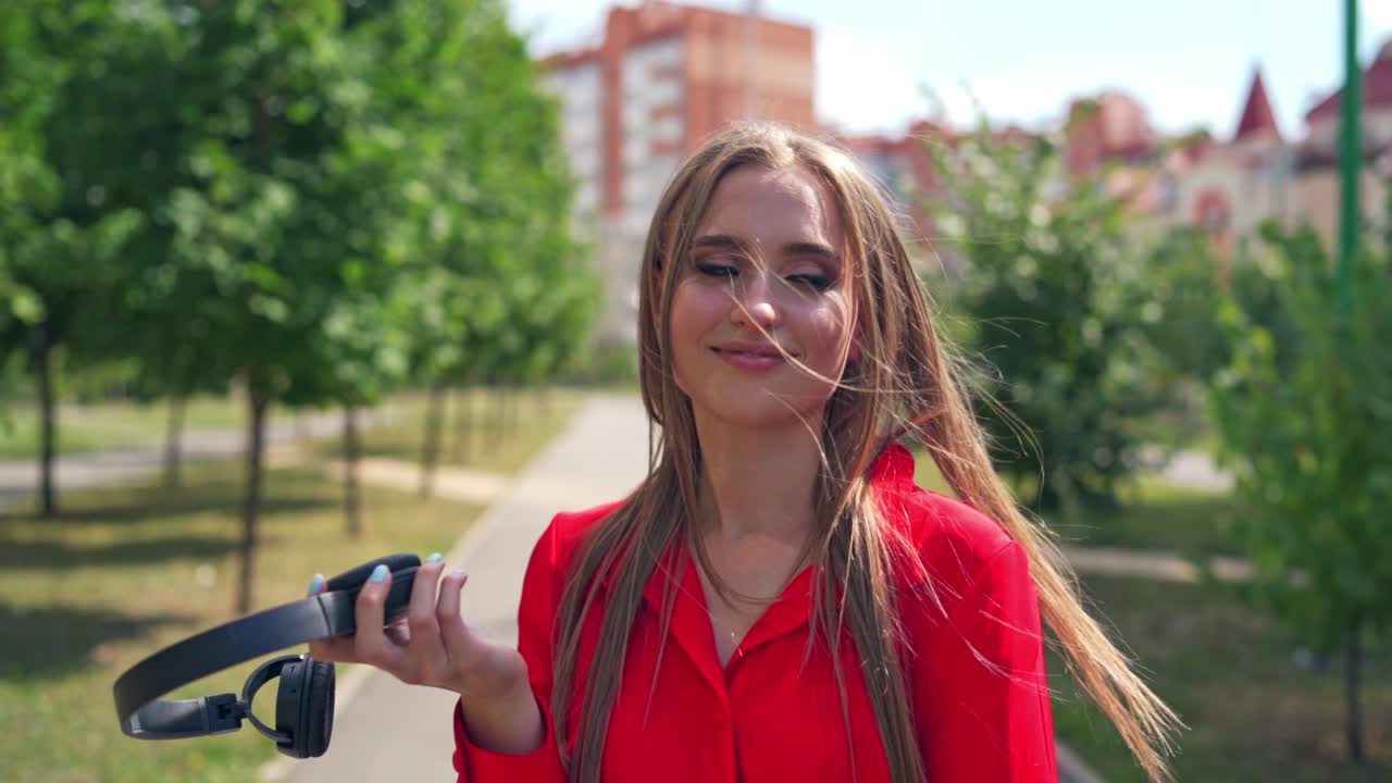 Beautiful girl with headphones walking in the city. Young woman with long hair listening to music through the headphones outdoors. Slow motion.