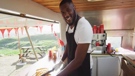 portrait of african american man smiling while preparing hot dogs in the food truck