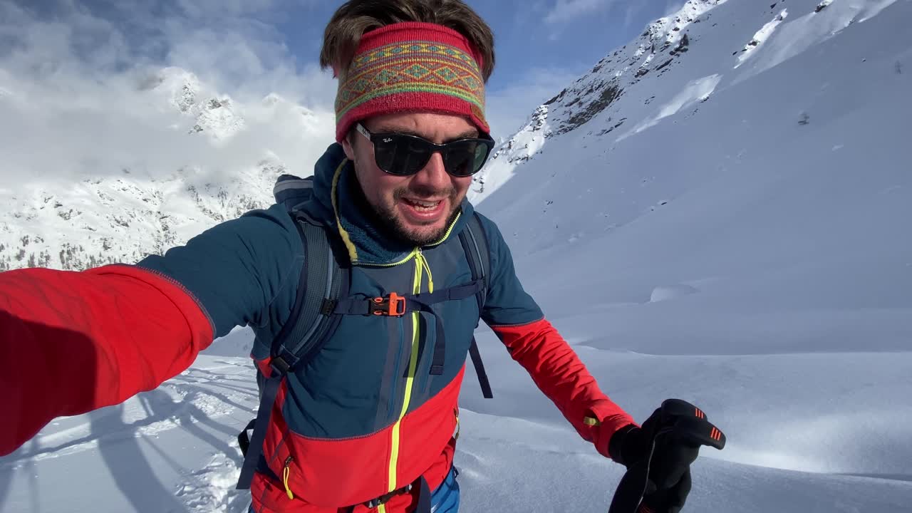 Giovane atleta che pratica sci alpinismo su un'alta montagna innevata mentre si filma.