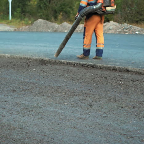 worker in protective clothes blows out the pieces of old asphalt from the pits at road construction site. road works concept. worker is using compressed air to blow off dust on the road.