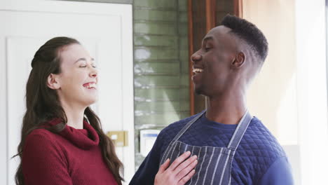 una pareja feliz y diversa de pie en la cocina, riendo y abrazándose, en cámara lenta.