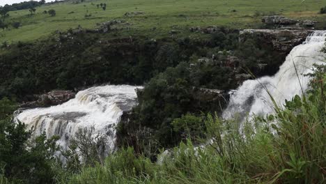 Toma-Estática-De-Hierba-Meciéndose-Con-El-Viento-En-Primer-Plano,-Con-Las-Cataratas-De-Lisboa-En-El-Fondo