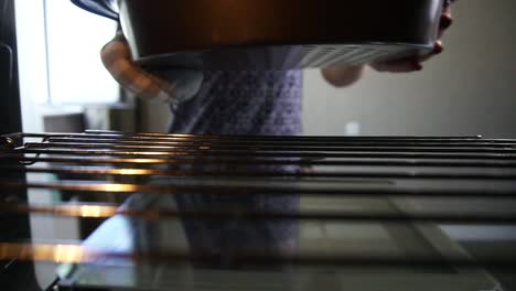 unrecognizable woman opens the oven's door and puts a baking pan with a cake inside: view from the oven. housewife cooking at