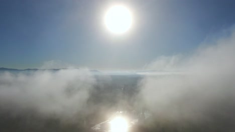 4k-Drohnenflug-Durch-Die-Wolken,-Direkt-Zur-Sonne-Und-Zum-See-An-Einem-Hellen-Tag