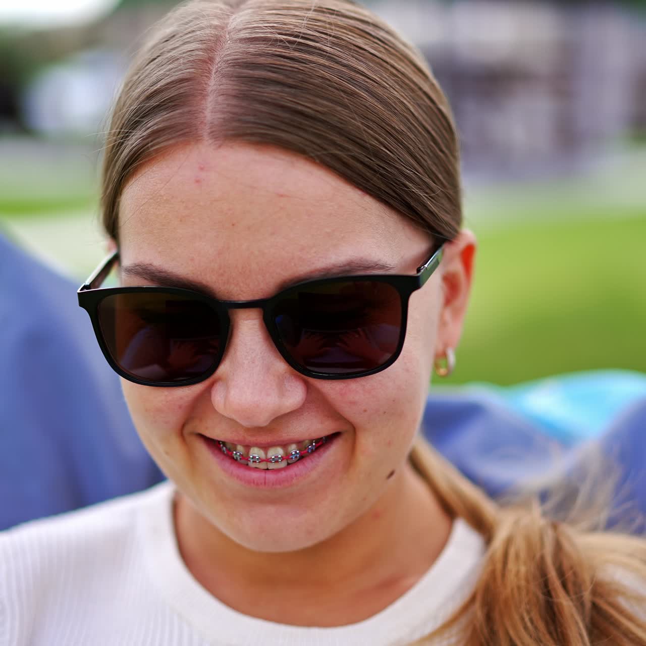 Happy relaxed young lady doing her job outdoors. Blonde lady in sunglasses sitting in bean bag chair working on laptop. Close up