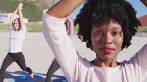 Afroamerikanische-Frau-Blickt-In-Die-Kamera-Und-Frauen-Dahinter-Am-Strand-Und-Blauer-Himmel-Im-Hintergrund